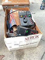 Box containing two black model train controllers and cords