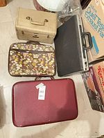 Four luggage pieces grouped: beige train case, floral attaché, metal briefcase, burgundy suitcase