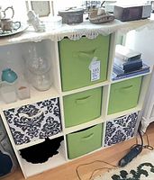 Full view of white 9-cube shelf with green and damask bins, garment steamer on floor
