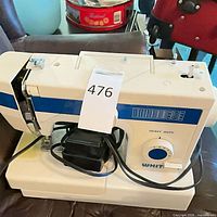 Top and side view of White sewing machine with attached cords and foot pedal