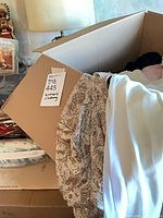 Box showing assorted women’s clothing with auction tag