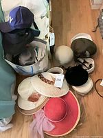 Group view of all hats including bag with caps and stack of straw and felt hats