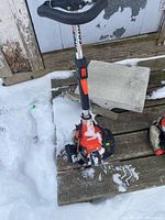 Red engine housing and shaft of gas trimmer on wooden surface with snow