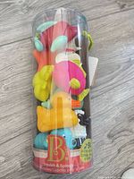 Front view of sealed tube containing nine colourful bath toys with B. Toys branding
