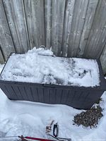 Closed brown plastic deck box covered with snow