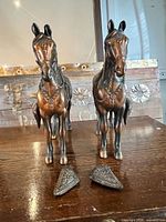 front view of two cast metal horse statues with detached panels on table