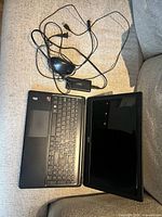 Open Acer laptop with power adapter and wired mouse on couch