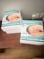 Two sealed packs of quilted crib mattress protectors on table