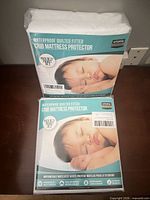 Two sealed packages of Utopia Bedding quilted fitted crib mattress protectors stacked