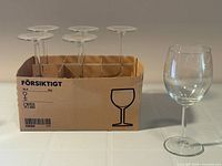Five glasses standing in original Ikea Forsiktigt six-cell cardboard box with one glass displayed outside for scale
