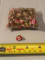 Bag of Canadian flag pins with one pin placed in front beside measuring tape