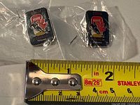 Two views of sealed rectangular lapel pin next to measuring tape showing size ~1.25 in.
