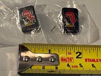 Two sealed IIHF 2009 Ottawa World Junior pins beside tape measure for scale