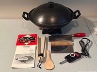 All items laid out including wok with lid, utensils, cookbook, power cord