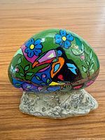 front view of painted rock on stone base showing toucan and flowers