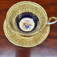 Teacup nested on saucer showing cobalt band, floral medallion and gilt pattern