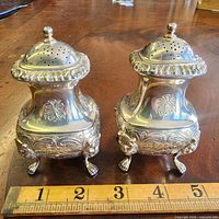 Front view of both Birks shakers showing ornate bodies, lion feet, ruler for scale