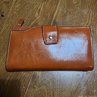 Closed cognac tan wallet showing exterior surface, snap-tab and top zipper pull