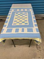 Blanket laid flat on table showing full top view with checkerboard centre and geometric border