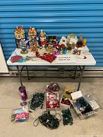 Full lot on table and floor showing village houses, Santa, tins, ornaments, garlands, and light strings