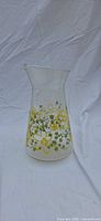Full view of clear glass Pyrex pitcher with yellow and olive green floral band