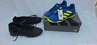 Black and blue Adidas indoor soccer shoes side by side; blue pair on box