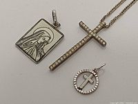 Three religious sterling silver items: cubic-zirconia cross pendant on chain, Virgin Mary rectangular pendant, circular cross pendant