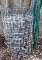 Rolled galvanized wire mesh fencing beside several green steel U-posts against wood fence