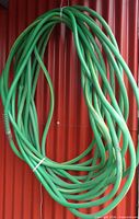 Full coil of green hose hanging against wall