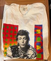 Front of folded white T-shirt showing Paul McCartney portrait and geometric graphics