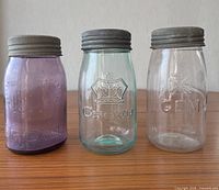 Front view of three antique mason jars showing colors, embossed logos and metal lids