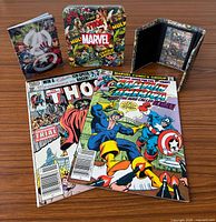 All items: two sleeved comics, metal tin, wallet, notebook on wood surface