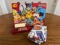 Group shot showing Pokémon art kit case, red calculator pencil box, folded Crayola sheet