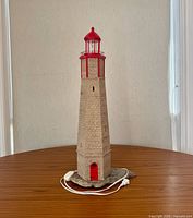 Front view of full lighthouse lamp showing tower, red lantern, rock base and cord