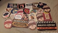 All 24 cardboard beer and cider coasters laid out face up showing brand graphics