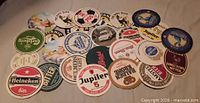 All 26 vintage beer advertising coasters spread out showing graphics and brands