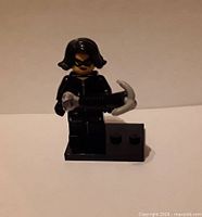 Front view of minifigure holding jewel and grappling gun on black stand