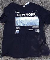 Front view of black New York skyline graphic T-shirt laying flat showing design and size tag visible