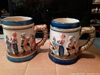 Front view of both porcelain beer mugs showing relief scenes and handles
