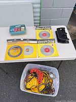 Tabletop view of packaged saw blades, hardware tray, black plastic stand, bin of cords