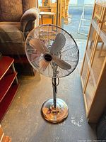 Full view of the Bionaire chrome pedestal fan standing on floor showing base, column, head and blades