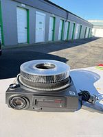 Projector with carousel tray and power cord on table outdoors