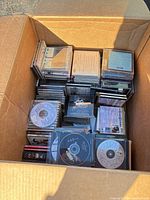 Open box filled with stacked jewel case CDs and loose discs