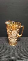 Front view of amber iridescent pressed glass pitcher with etched floral motif