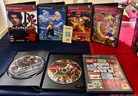 All seven PS2 game cases displayed; two cases open showing God of War disc 1 and GTA III disc; God of War II special features disc also visible
