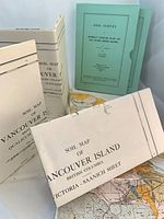 Group view of folded soil maps, green survey report folders, showing titles and partial coloured map