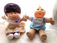 Both dolls seated side by side showing outfits and size