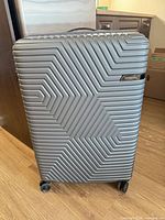 Front view of silver American Tourister hardside suitcase showing geometric texture and spinner wheels