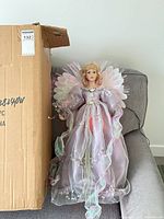 Full view of doll seated beside carton showing overall size and lavender dress