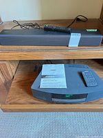 Sony soundbar on shelf with remote resting on top, Bose Wave unit below with manual and remote